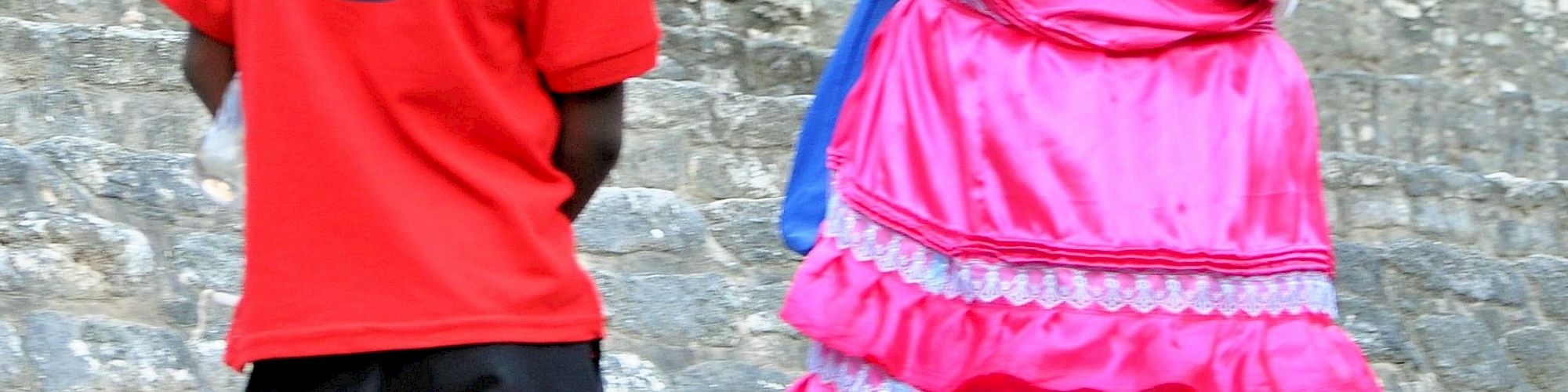 A woman in a traditional outfit and a boy in a red shirt are standing on stone steps, appearing to engage in conversation.