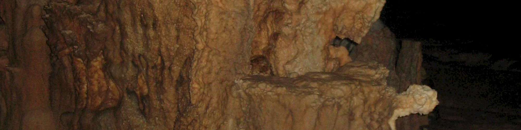 This image shows a cave formation featuring stalagmites and stalactites, with intricate shapes and textures. A human figure is visible in the background.