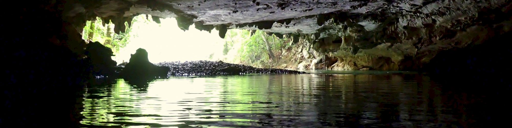 The image shows the interior of a cave with water at the bottom, partially illuminated by natural light entering from the cave's opening.