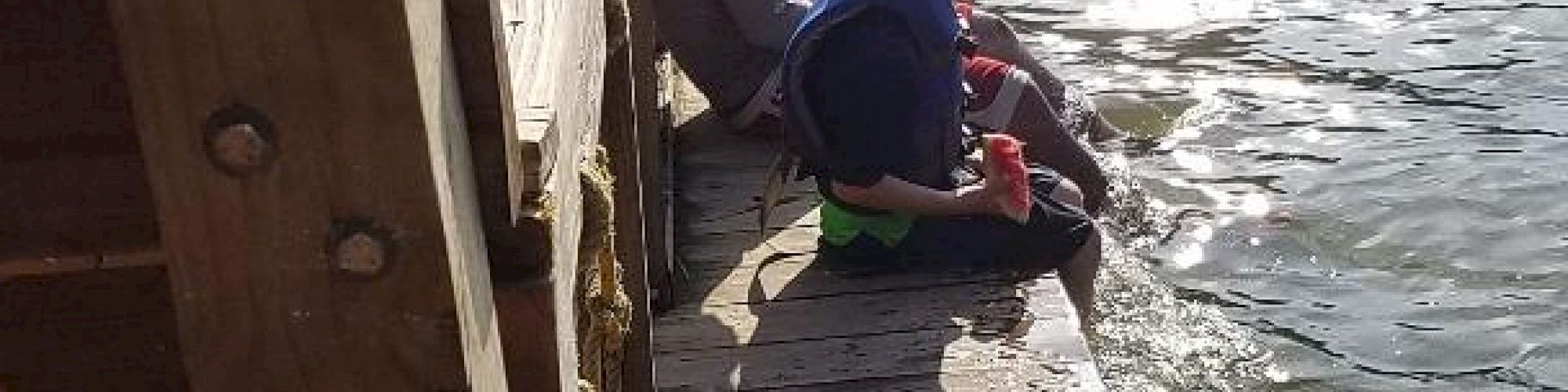 A man and a child sit on a wooden platform by the water, enjoying the view of the river under sunny skies.