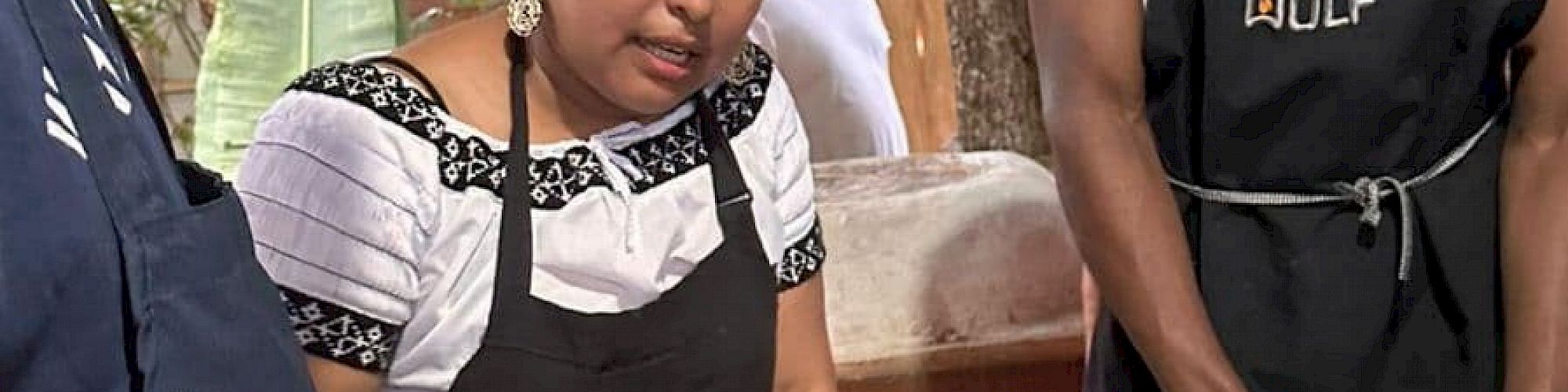 People are cooking together, preparing food around a table with various ingredients and tools.