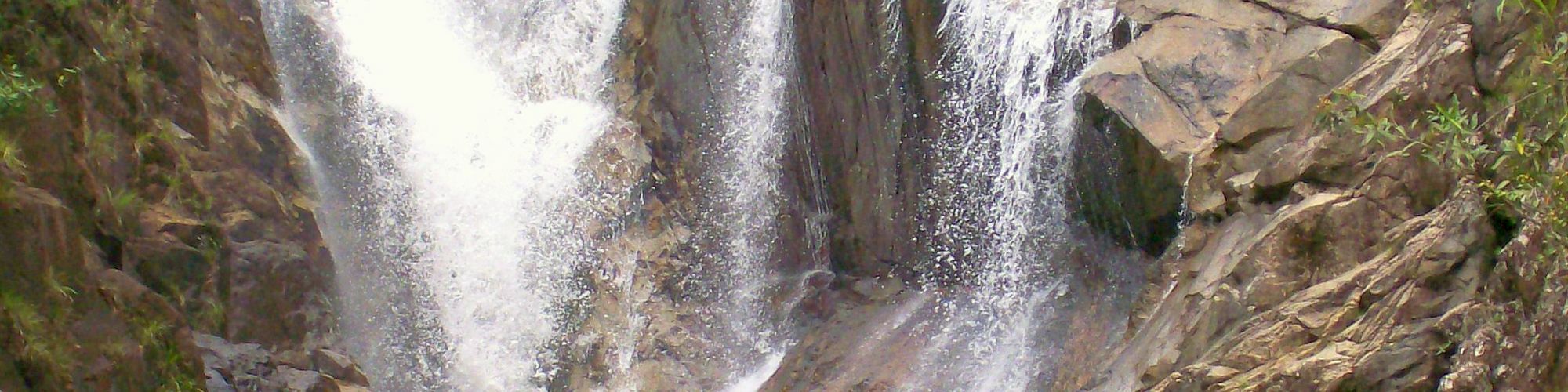 A waterfall cascades down rocks into a pool below, with a few people visible at the base enjoying the natural scenery.