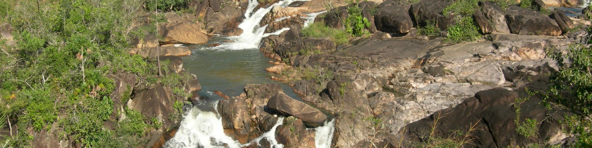 This image shows a scenic view of a small waterfall cascading over rocks in a lush, green forested area.