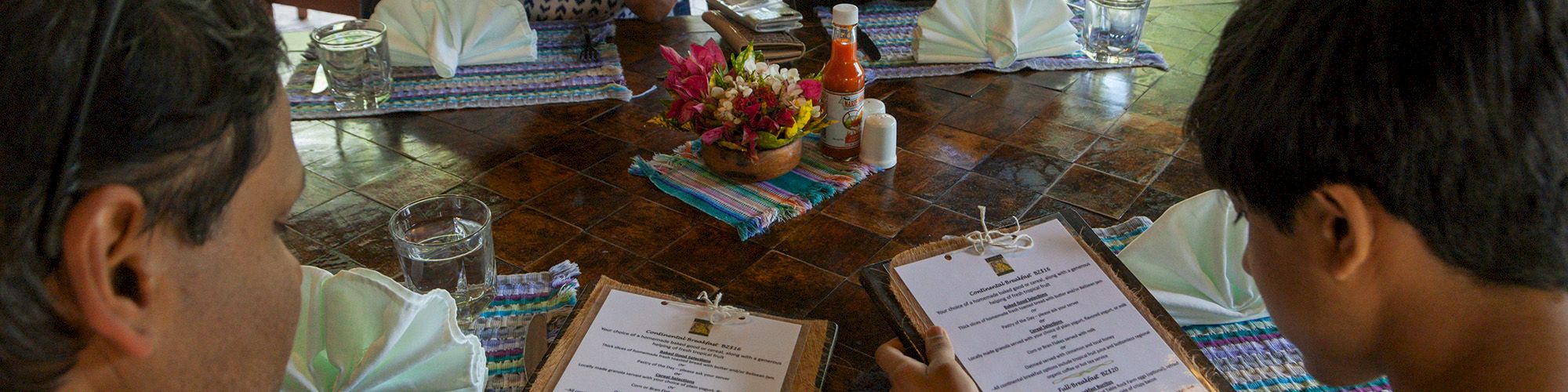 Four people sit at a restaurant table, looking at menus, with utensils and table settings ready for a meal.