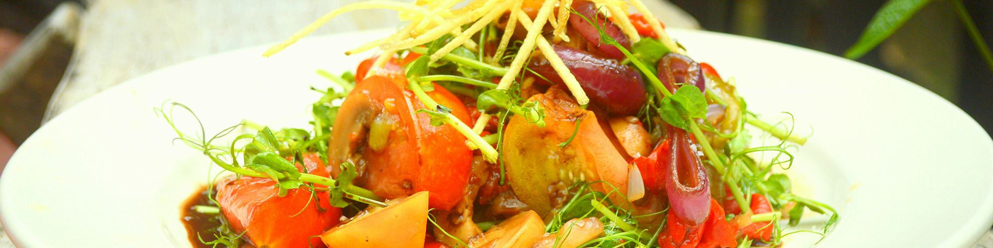 The image shows a plated dish of vegetables and greens, topped with crispy fried potato sticks, presented on a wooden surface.