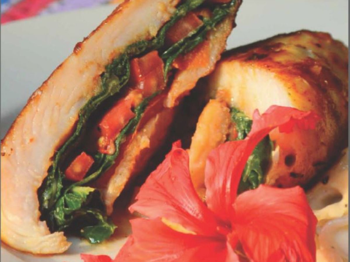 The image shows a gourmet dish with stuffed chicken, garnished with greens and a hibiscus flower, served on a white plate.