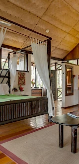 This image shows a cozy, well-decorated bedroom with a four-poster bed, a sofa, wooden furniture, and a warm, inviting atmosphere.