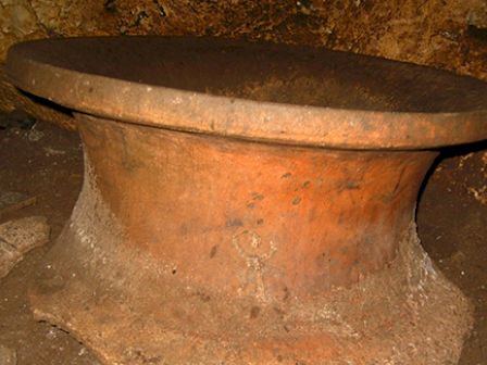 This image shows an old, round, and weathered stone structure or possibly an artifact with a flat top, situated in a rough, earthy environment.