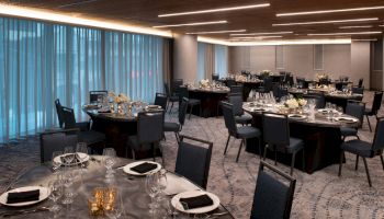 This image shows an elegantly arranged banquet room with round tables set for a formal dining event, featuring black chairs and dark tablecloths.