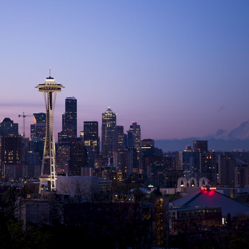 The image depicts the skyline of Seattle at dusk, featuring the iconic Space Needle and Mount Rainier in the background.