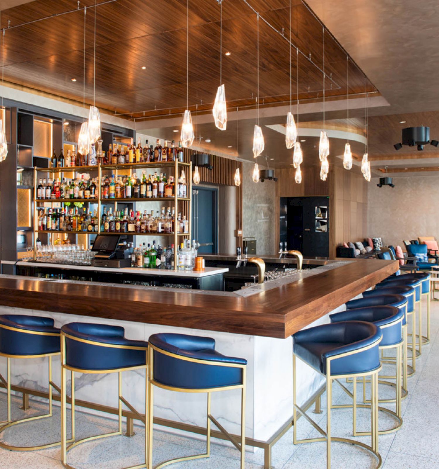 This image shows a modern, well-lit bar with stylish seating, a wide selection of bottles behind the counter, and contemporary decor.