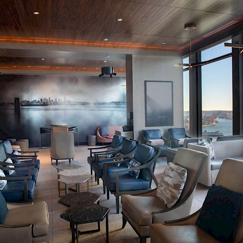 A spacious lounge with modern seating, a panoramic city mural, and large windows offering a scenic view of a waterfront and a Ferris wheel.