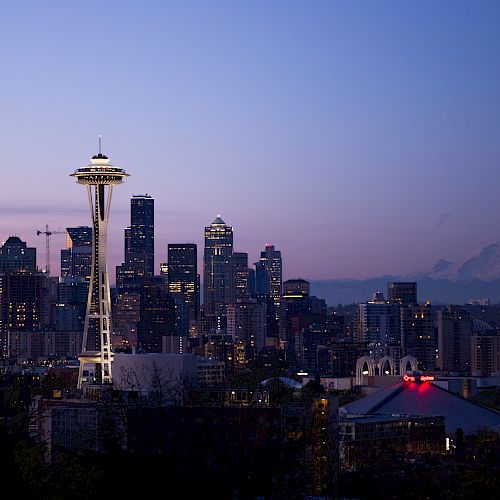 The image depicts the Seattle skyline at dusk, featuring the Space Needle prominently in the foreground with Mount Rainier in the background.