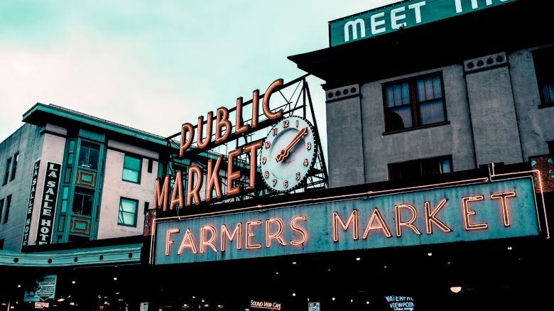 The image shows the iconic "Public Market" and "Farmers Market" signs at a well-known market, with a clock and adjacent buildings in the background.
